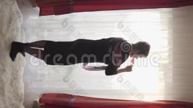 垂直拍摄优雅的白种人黑发女人喝红酒在地板前到天花板窗口。 优雅优雅